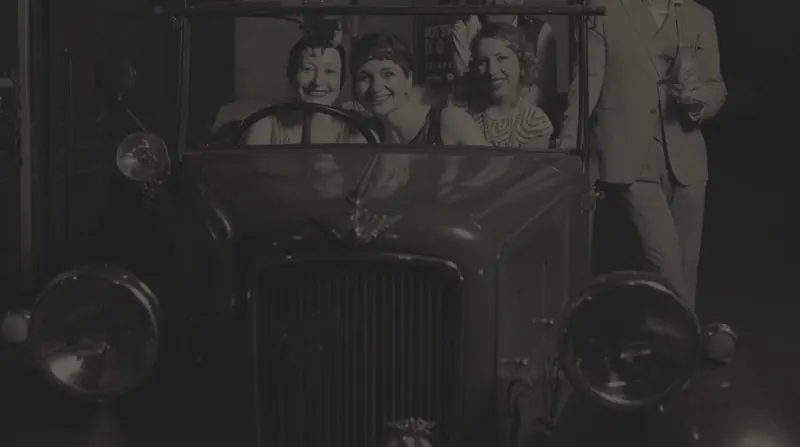 Tre ragazze in abiti anni '20 su un'auto d'epoca