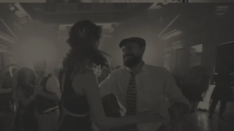 Una coppia balla sorridendo, lui con coppola e cravatta